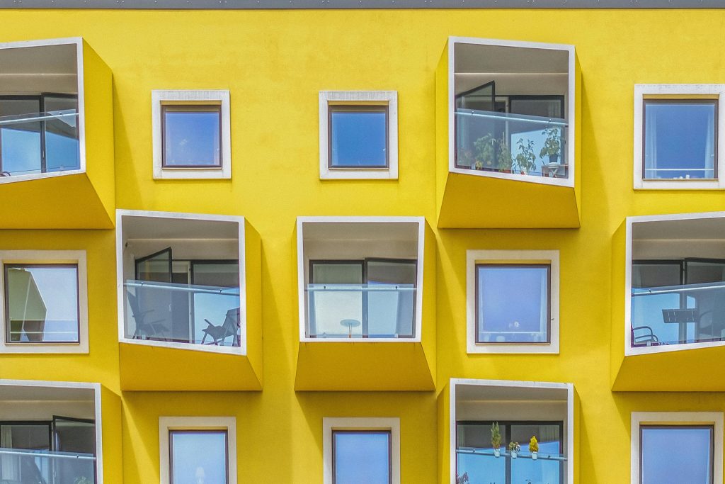 Contemporary yellow building facade with geometric balconies and glass windows.