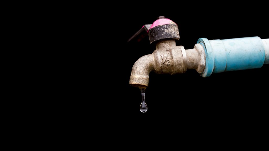 A detailed view of a metal faucet with a single water drop against a black background.